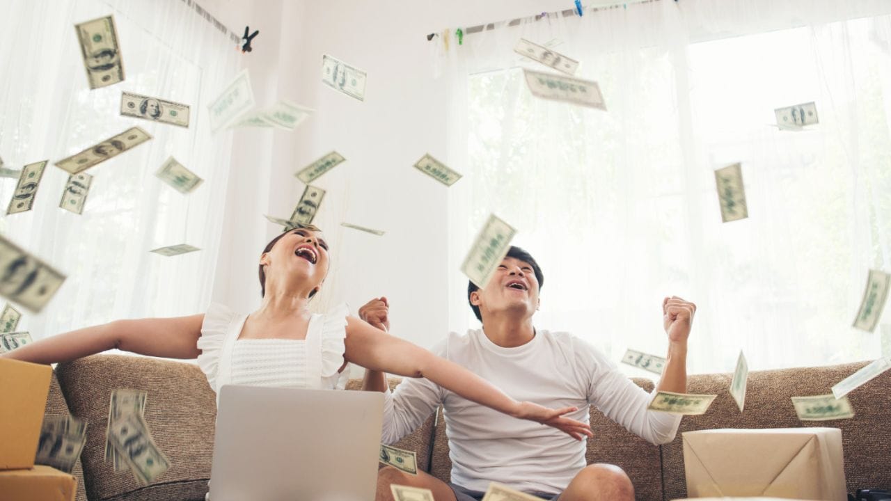casal recebendo chuva de dinheiro sentado no sofá da sala